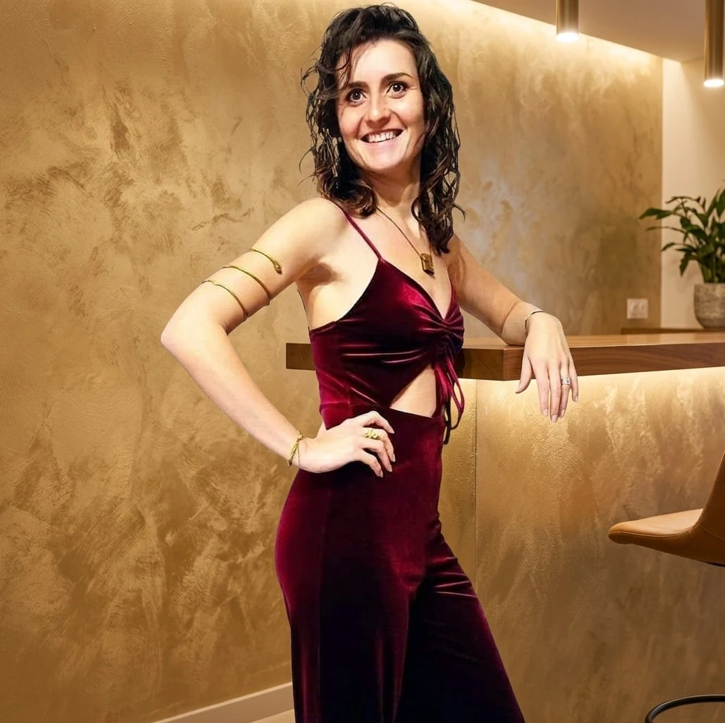 Portrait de Mathilde Régnier souriante, portant une robe bordeaux dans un intérieur chaleureux.